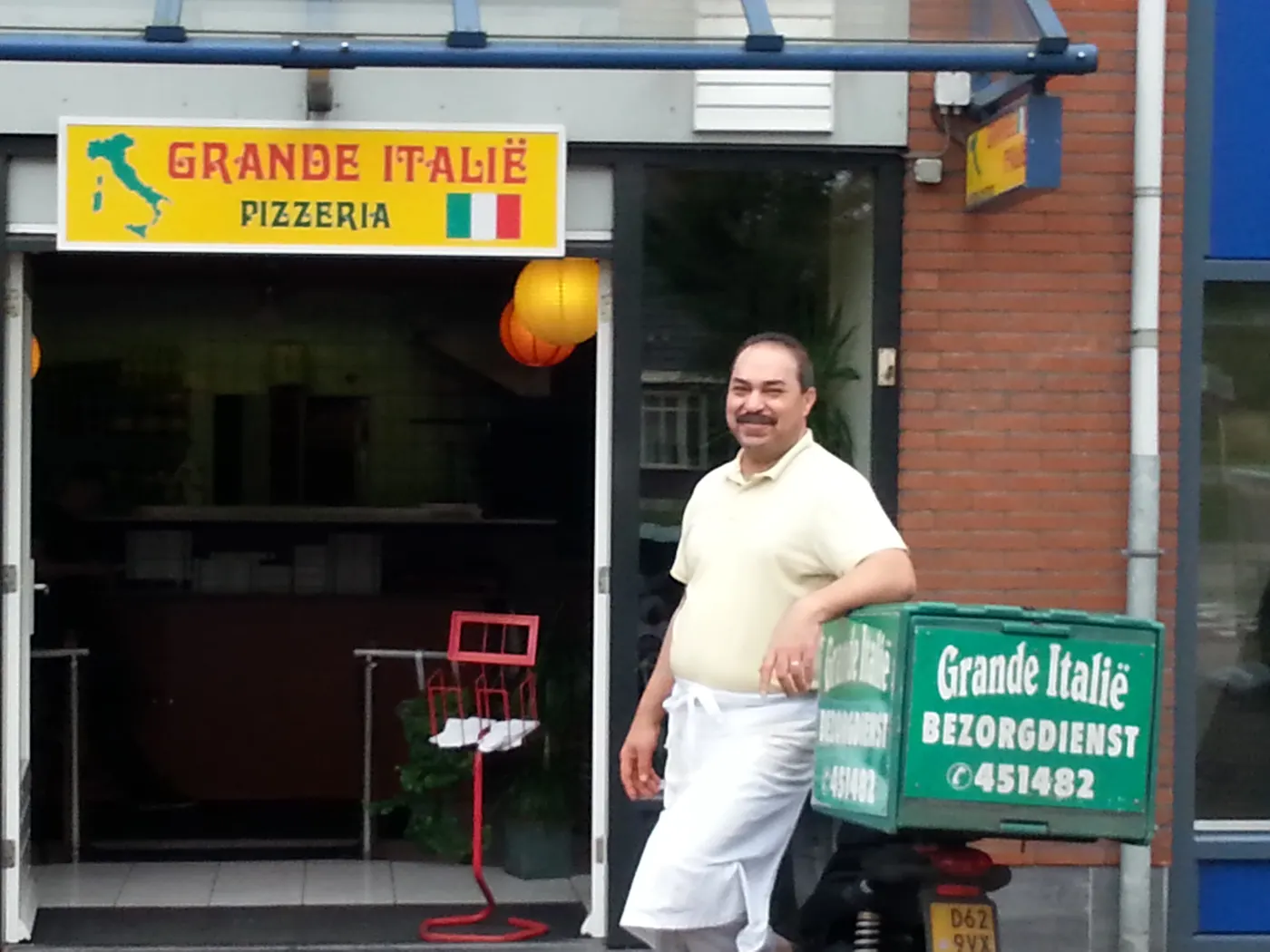 Mario voor de gevel van Grande Italië met de bezorgscooter.