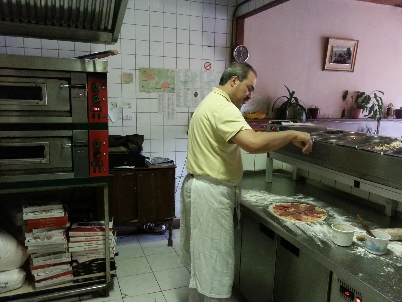 Mario belegt een verse pizza aan de werkbank.