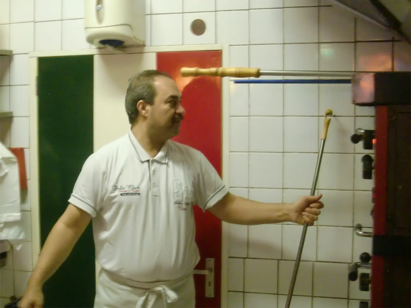 Mario met de pizzaschep bij de oven.